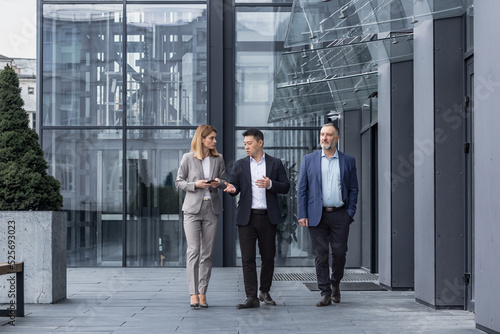 Three diverse business people walking and talking focused and thoughtful seriously outside office building, male and female, discussing plans and work project © Liubomir