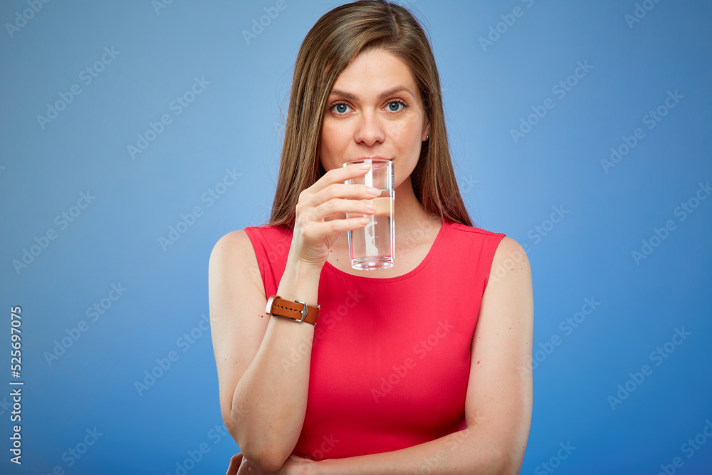Woman in red dress drinking water from glass. Isolated female person portrait on blue background. Woman in red dress drinking water from glass. Isolated female person portrait on blue background.
