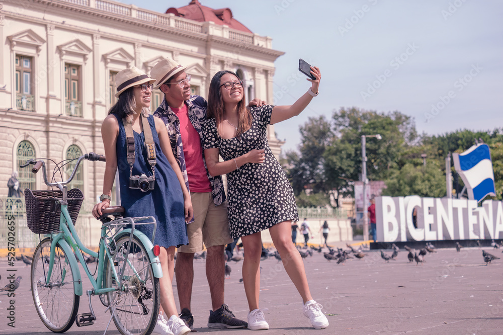 Obraz premium Happy tourists taking selfies with smartphones in a park in downtown El Salvador. Hispanic people.