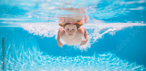 Young boy swim and dive underwater. Under water portrait in swim pool. Child boy diving into a swimming pool. Summer vacation concept.