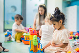 Learning through play at the nursery school. Little girl, other toddlers and their teacher playing with colorful plastic playhouses, building blocks, cars and boats. Imagination, creativity, fine