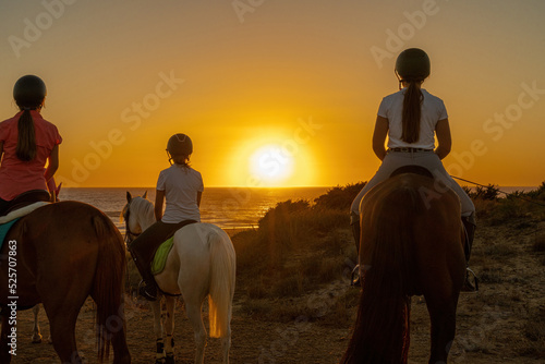 several young riders watch the sunset on the sea above a hillside photo