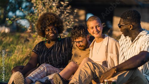 Group of happy young people having a weekend picnic in nature, sitting together on the grass near the campfire, talking and laughing. Sunset time. High quality photo