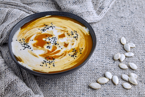 A plate of creamy pumpkin soup with cream and black cumin and pumpkin seeds on a light knitted wool sweater