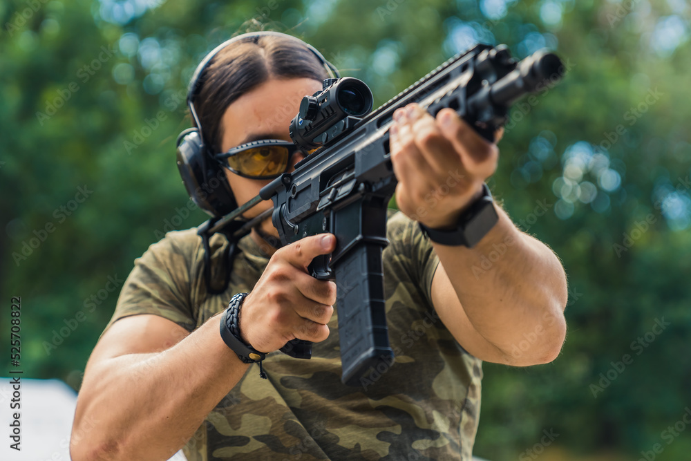 Military concept. Middle-aged European white black-haired man focused on aiming at target via rifle loupe. Medium closeup shot. Blurred trees in the background. High quality photo