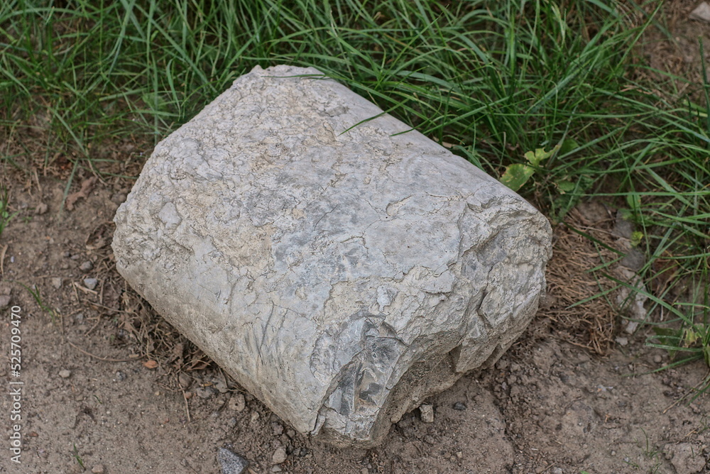 one gray concrete piece lies on the ground in the green grass on the street one gray concrete piece lies on the ground in the green grass on the street