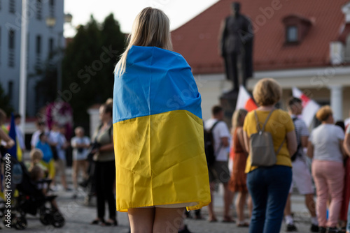Konstfotografi In focus: migrant blond woman stands in crowd (square) and covers shoulders by Ukrainian blue and yellow flag