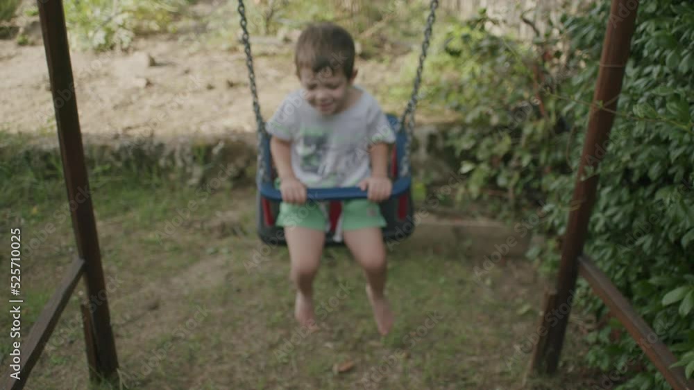 Happy child swings on a house swing. Smiling child plays in the garden with a swing Happy child swings on a house swing. Smiling child plays in the garden with a swing