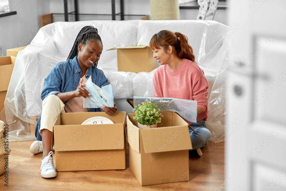 moving, people and real estate concept - women unpacking boxes at new home or packing stuff into bubble wrap moving, people and real estate concept - women unpacking boxes at new home or packing stuff into bubble wrap