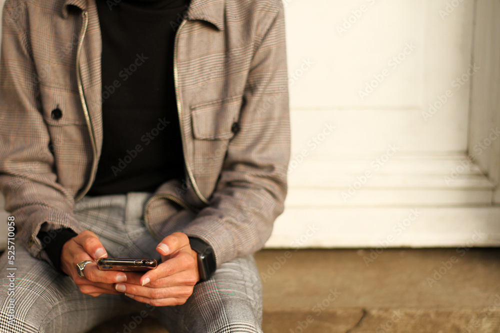 young man using his smart cell phone while sitting on a staircase sending messages
