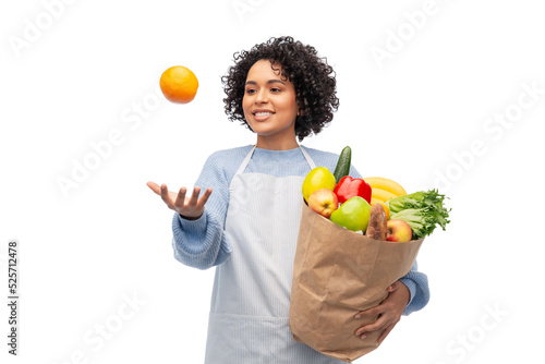 cooking  delivery and people concept - happy smiling woman in apron holding takeaway food in paper bag and throwing orange in air over white background