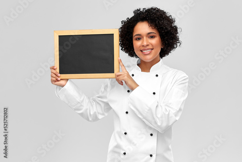 cooking, advertisement and people concept - happy smiling female chef in white jacket holding black chalkboard over grey background
