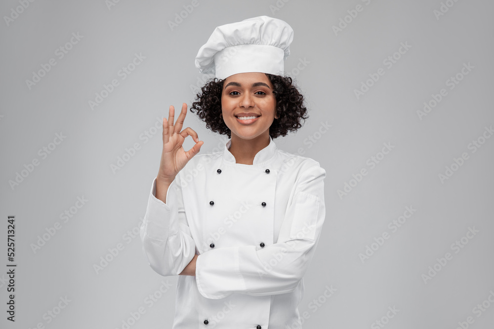 cooking, culinary and people concept - happy smiling female chef in toque showing ok hand sign over grey background cooking, culinary and people concept - happy smiling female chef in toque showing ok hand sign over grey background