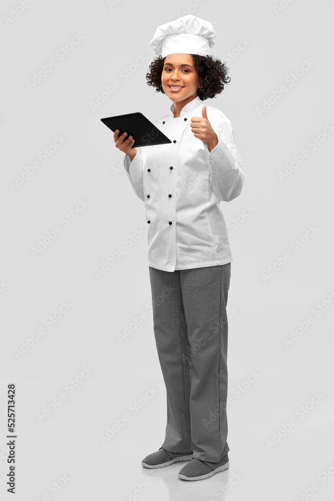cooking, culinary and people concept - happy smiling female chef in toque and jacket with tablet pc computer showing thumbs up over grey background cooking, culinary and people concept - happy smiling female chef in toque and jacket with tablet pc computer showing thumbs up over grey background