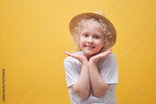 cute little girl in a white t-shirt having fun, a child in a straw hat on a yellow background