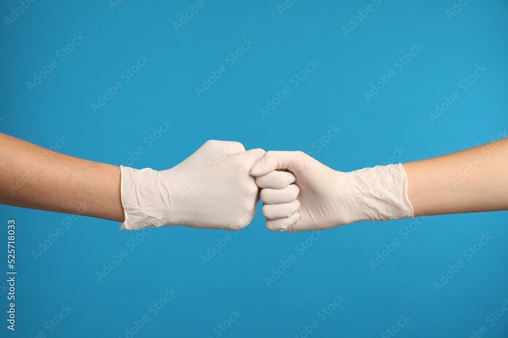 Fototapeta premium Doctors in medical gloves making fist bump on light blue background, closeup