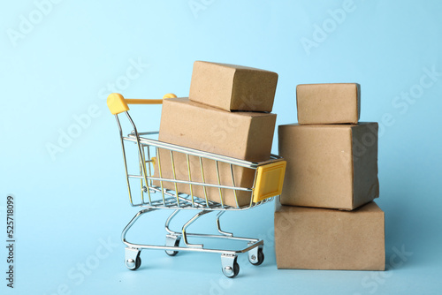 Shopping cart and boxes on light blue background. Logistics and wholesale concept