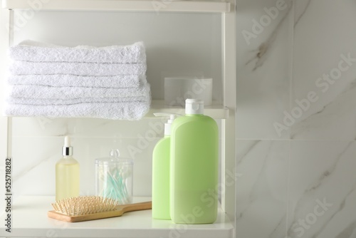 Stack of towels, hairbrush, shampoo and other toiletries on shelves near white marble wall