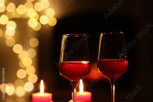 Glasses of wine and candles against blurred lights, closeup with space for text. Romantic dinner