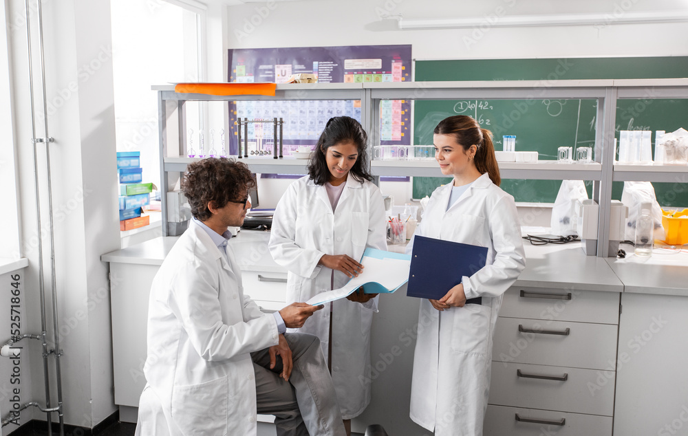 science research, work and people concept - international group of happy scientists with folder discussing report in laboratory science research, work and people concept - international group of happy scientists with folder discussing report in laboratory