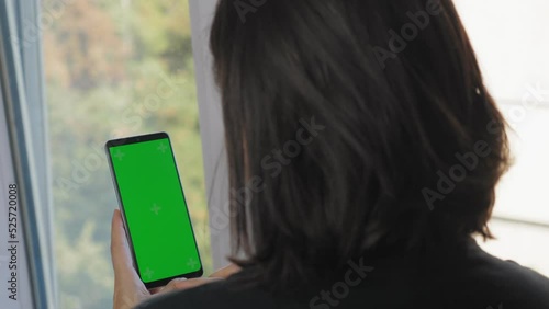 A girl with short dark hair stands with her back to the camera and holds a phone with a green screen. A woman makes purchases on the site using the phone. 