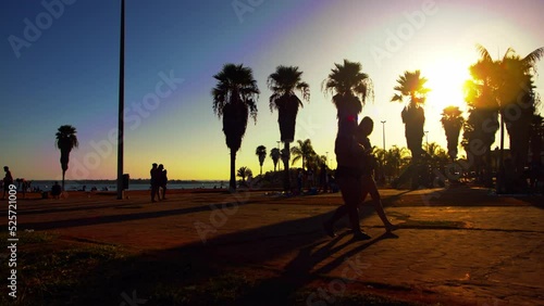 Silhouette of people walking on ocean side broadwalk during sunset in Brasilia, Brazil. Palm trees in background photo