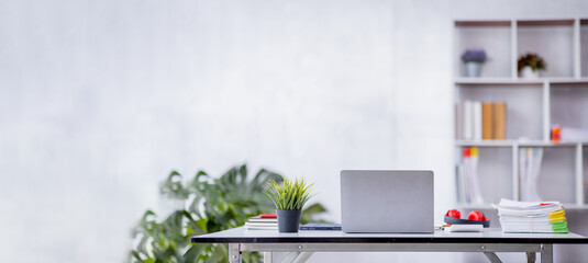 Contemporary workspace with laptop computer notebook, and supplies on wooden table desk in a large open plan office space after working hours, panoramic view.