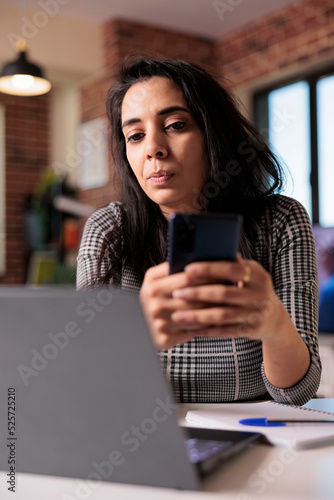 Student employee browsing internet on smartphone, using social media app to text messages on work break at home. Working on remote job with laptop and mobile phone, searching online information.