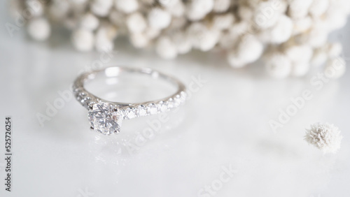 Close up of diamond ring with white flower, sunlight and shadow background. Love, valentine, relationship and wedding concept. Soft and selective focus. photo
