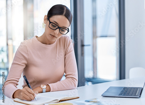 Planning, thinking and strategy with business woman writing notes while working on a laptop in a corporate office. Professional assistant plan schedule and meetings, using journal to write reminder