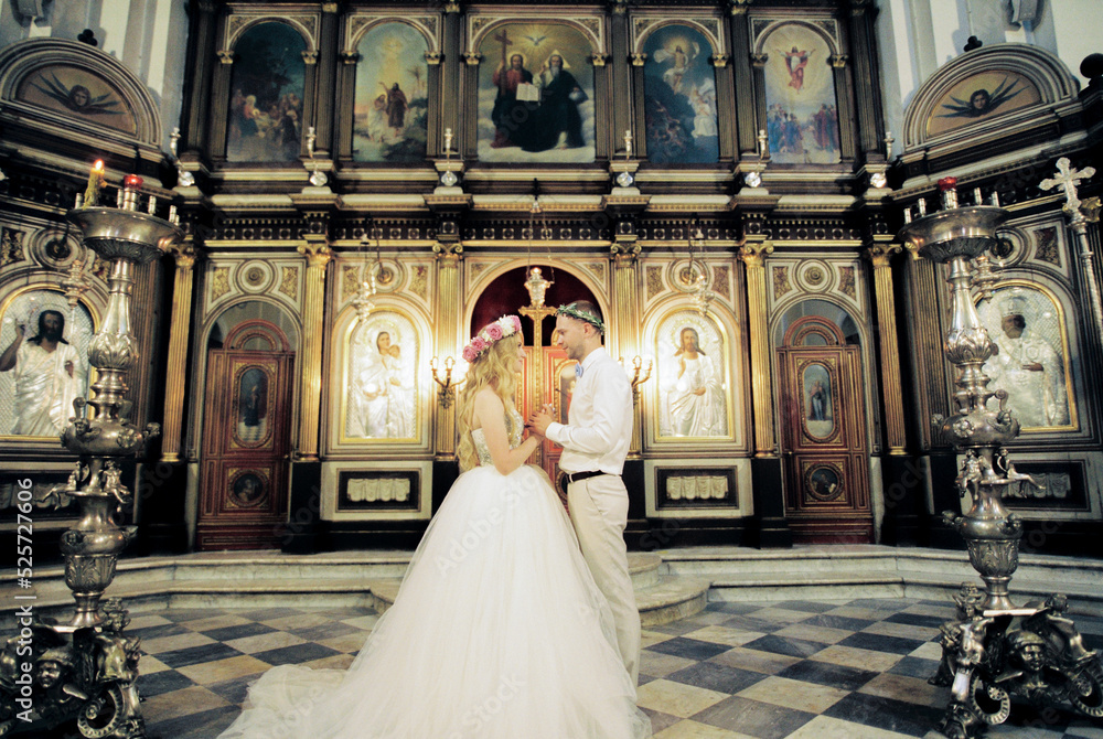 Bride and groom stand in the church in front of the iconostasis holding hands
