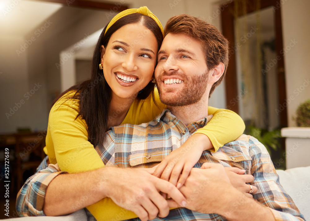 © N Felix/peopleimages.com - Happy and excited couple hugging thinking of future relaxing and sitting on a couch at home. Relaxed diverse interracial lovers smiling and enjoying quality time together and having fun in the house