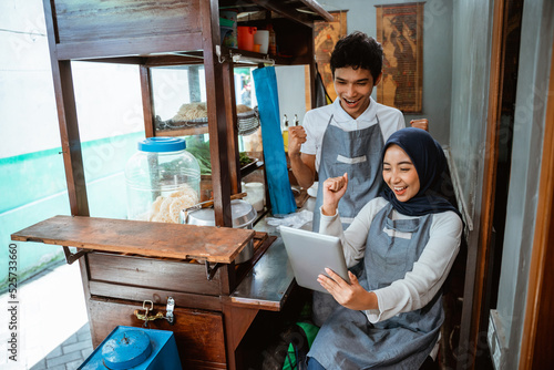 a couple of sellers in aprons were surprised with fists clenched up when seeing a tablet in a stall cart photo