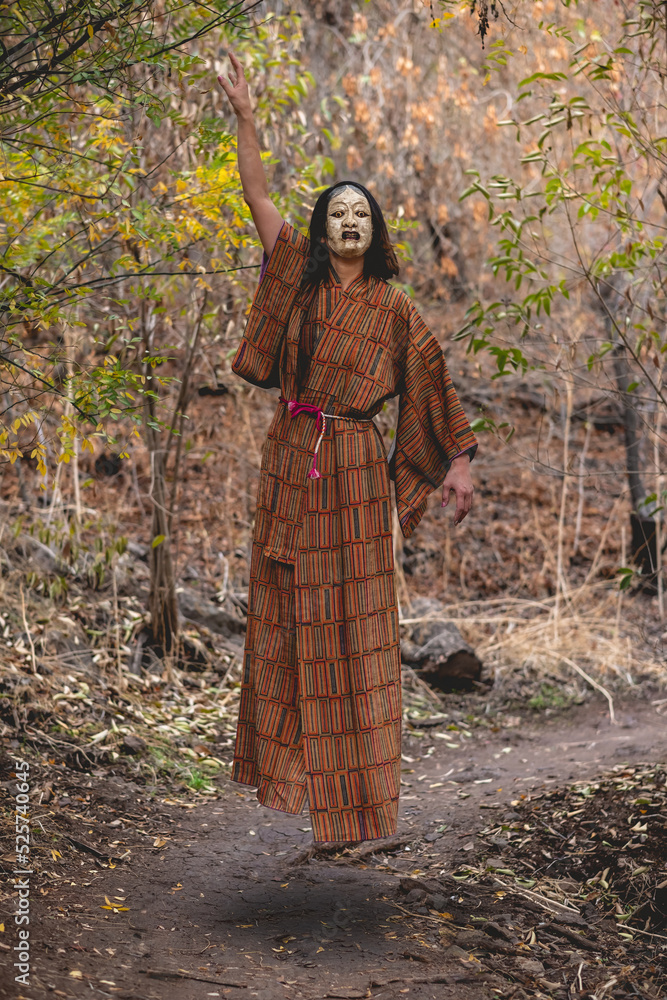 Paranormal portrait of sexy and young japanese woman with beautiful old traditional brown and orange kimono and traditional noh mask floating in the autumn forest