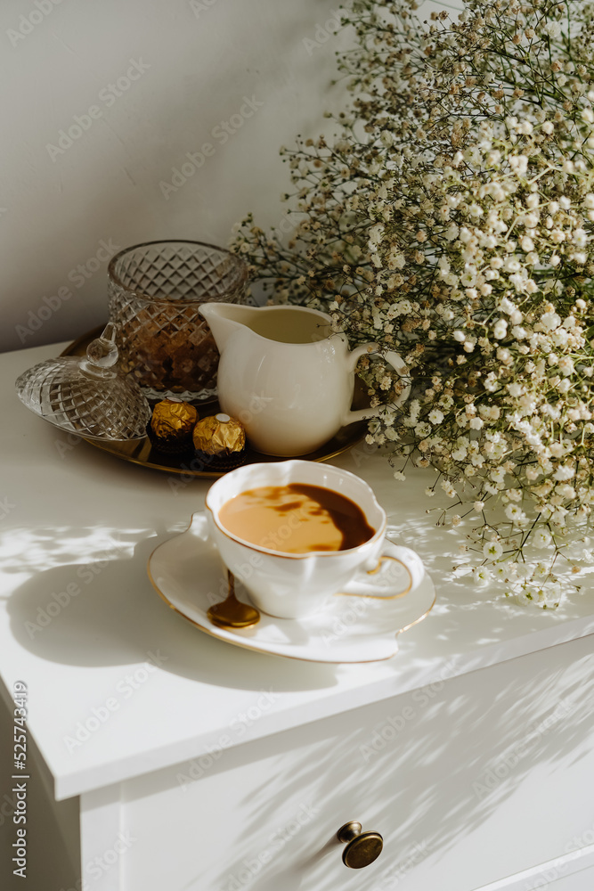 Fototapeta premium A bouquet of flowers, a cup of tea or coffee with milk and sweets on the table. Feels like home comfort and minimalism. aesthetic. 