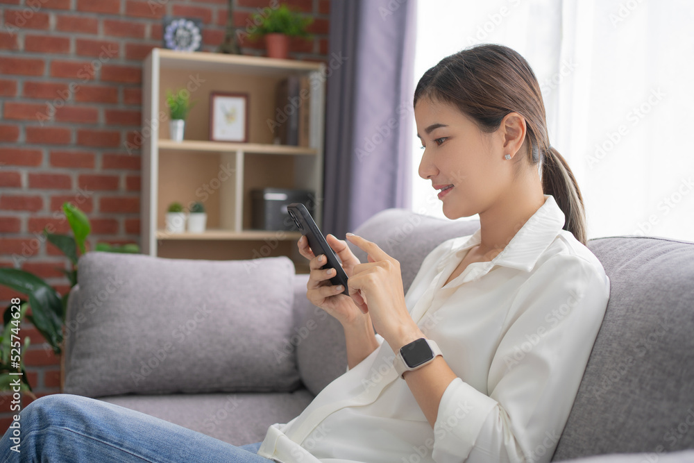 Portrait of a happy young Asian woman using a smartphone in living room at condominium Portrait of a happy young Asian woman using a smartphone in living room at condominium
