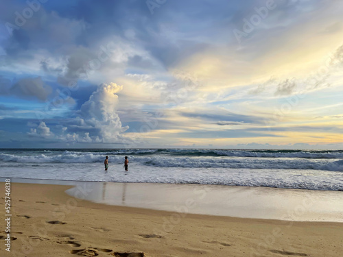 Beach and sunset. Amazing beautiful sky with sun glow and pattern of clouds. Two men stand in the sea in shallow and talk with each other. Clean yellow sand with footprints. Awesome beauty of nature. photo