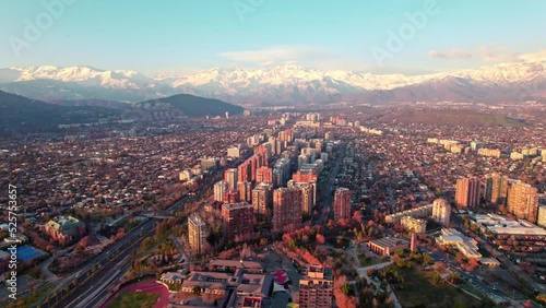 Aerial dolly in of Las Condes neighborhood buildings, snow capped mountains in background at sunset, Santiago, Chile photo
