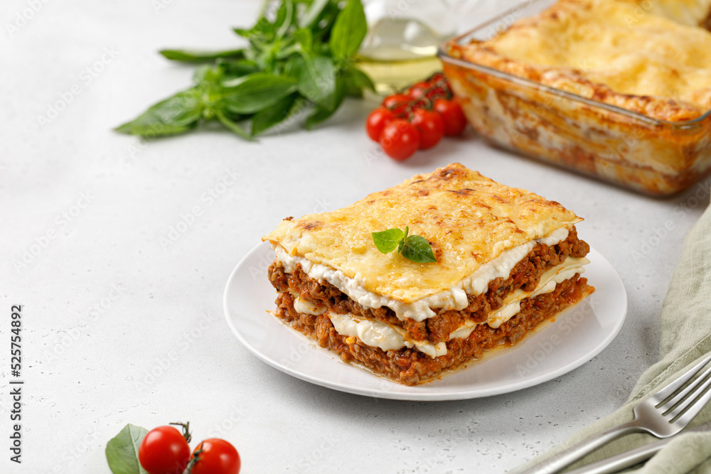 Delicious Lasagne with bolognese meat sauce and cheese on white plate with fork and knife. Traditional Italian lasagna. Copy space.