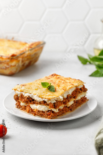 Delicious Lasagne with bolognese meat sauce and cheese on white plate and grey background. Traditional Italian lasagna. © Maria