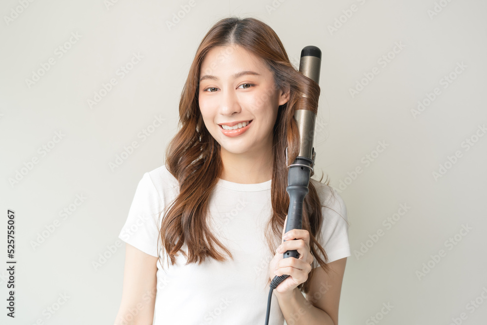 Beautiful curly brunette, attractive asian young woman, girl smiling using curler, curling iron long hair with ceramic curler straightener at home. Hairstyle and Hairdressing. Beauty and hair care . Beautiful curly brunette, attractive asian young woman, girl smiling using curler, curling iron long hair with ceramic curler straightener at home. Hairstyle and Hairdressing. Beauty and hair care .