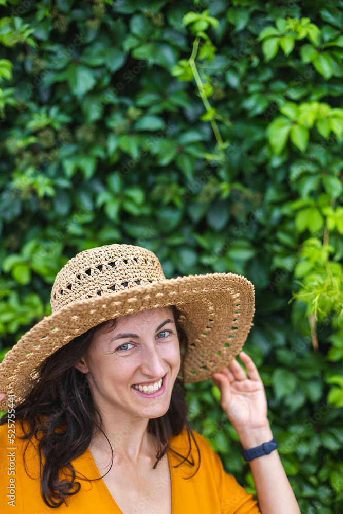 A smiling girl in a straw hat stands near a wall overgrown with ivy