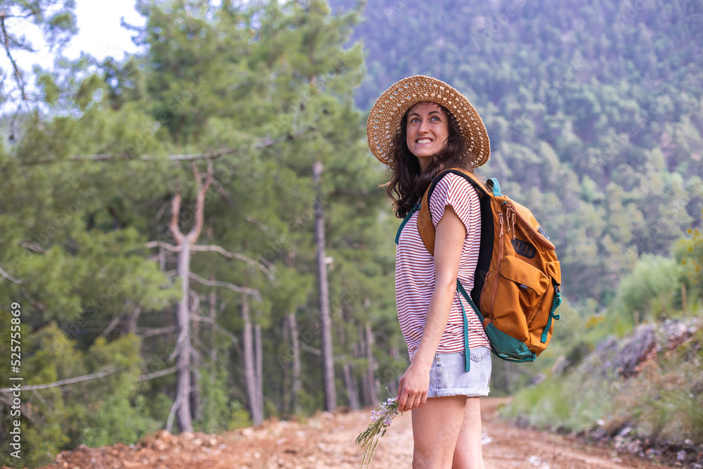A woman with a backpack and a straw hat on a mountain path