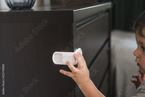 Child unsupervised plays with cabinets. Danger for the baby to pinch the hand of the cabinet door. Protect children from home furniture kids safety. Selected focus photo
