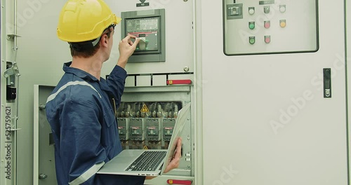 Professional inspector electrician technician engineer in safety uniform helmet hat holding laptop checking power voltage electrical system control panel at industrial factory construction site