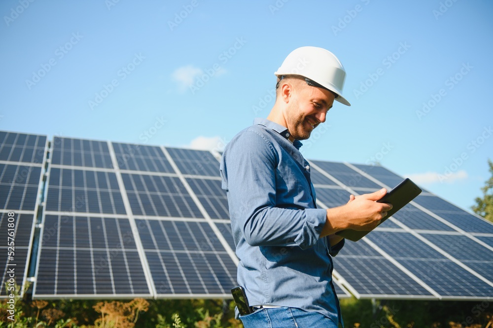 The portrait of a young engineer checks with tablet operation with sun, cleanliness on field of photovoltaic solar panels. Concept: renewable energy, technology, electricity, service, green power The portrait of a young engineer checks with tablet operation with sun, cleanliness on field of photovoltaic solar panels. Concept: renewable energy, technology, electricity, service, green power