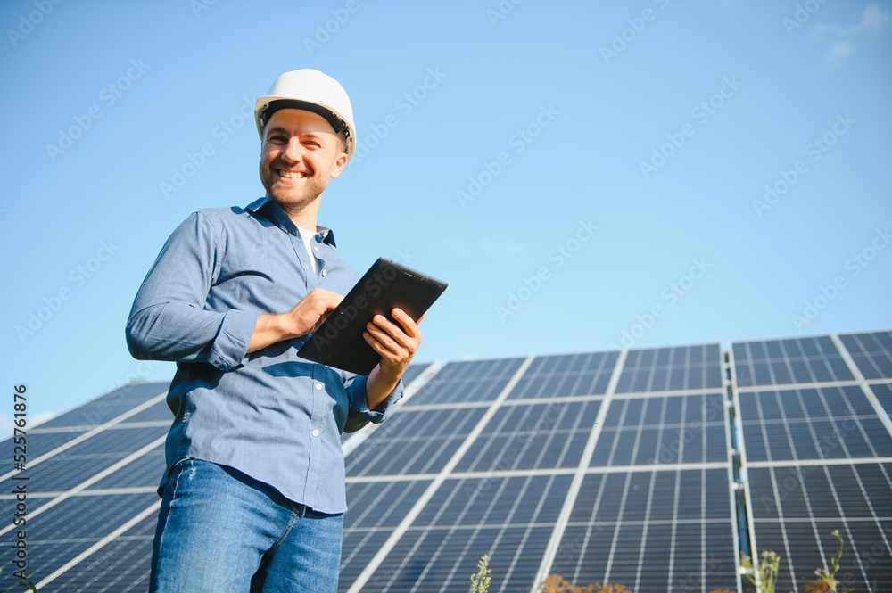 The portrait of a young engineer checks with tablet operation with sun, cleanliness on field of photovoltaic solar panels. Concept: renewable energy, technology, electricity, service, green power The portrait of a young engineer checks with tablet operation with sun, cleanliness on field of photovoltaic solar panels. Concept: renewable energy, technology, electricity, service, green power