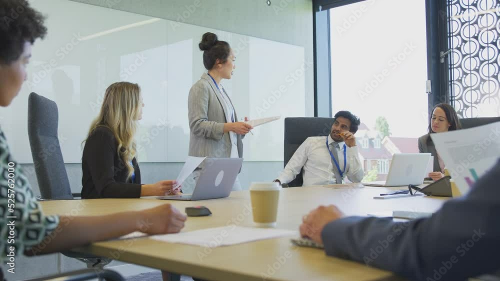 Businesswoman standing and leading colleagues sitting around boardroom table in meeting - shot in slow motion Businesswoman standing and leading colleagues sitting around boardroom table in meeting - shot in slow motion
