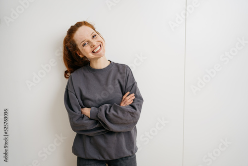 young redhead woman stands laughing with folded arms in front of white wall