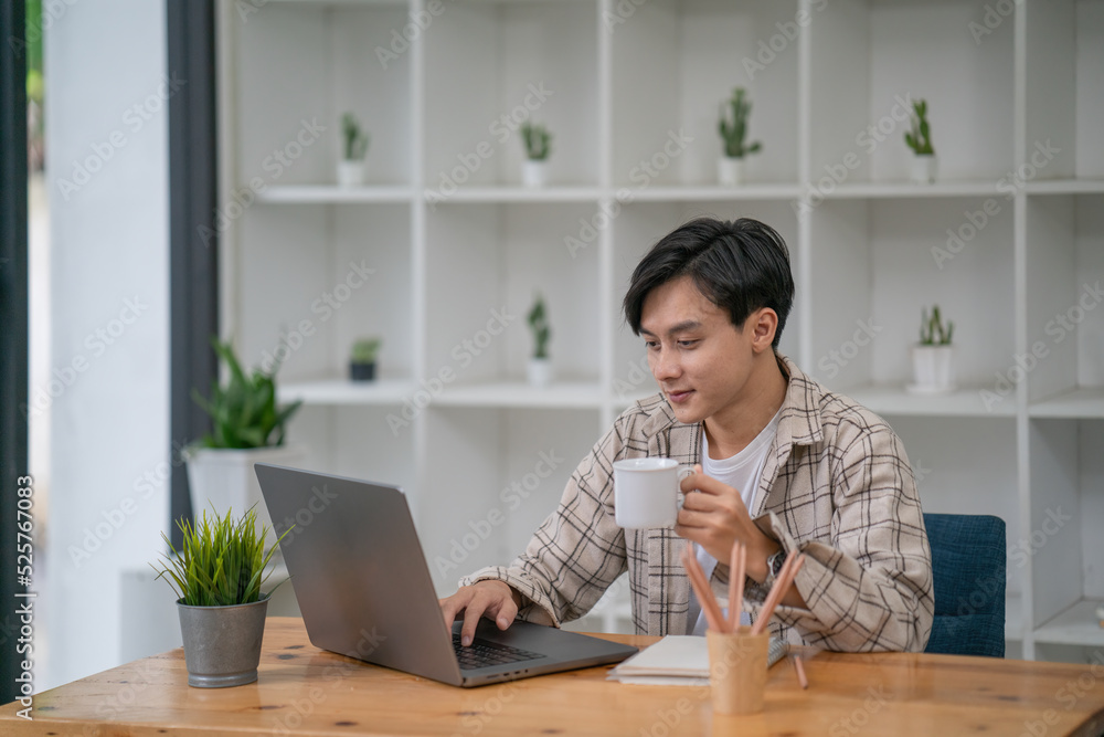 Asian businessman holding a coffee mug working on laptop at office. Asian businessman holding a coffee mug working on laptop at office.